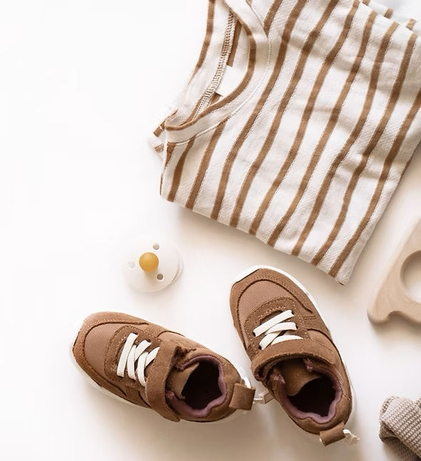A folded striped baby romper with tan shoes, a dummy and a wooden teether