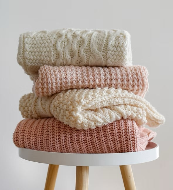 A stack of knitted baby blankets in cream and blush on a small round table