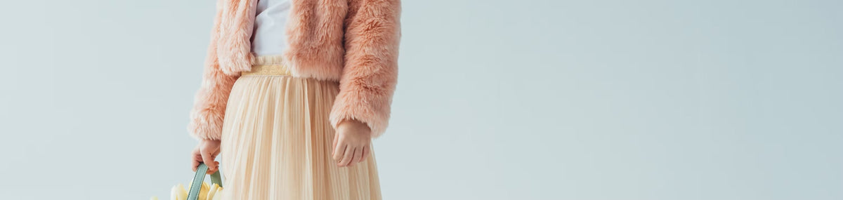 A child in a pink jacket and cream tulle skirt holding flowers
